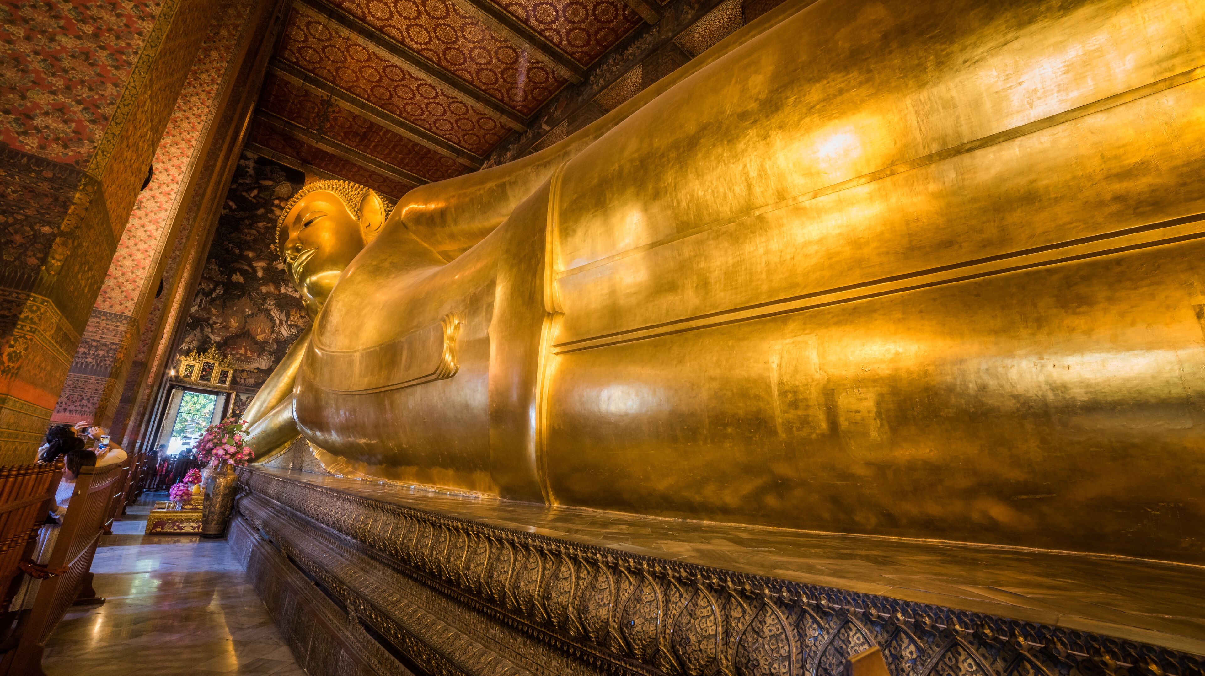 A large golden Buddha statue in a temple with intricate carvings and a patterned ceiling.