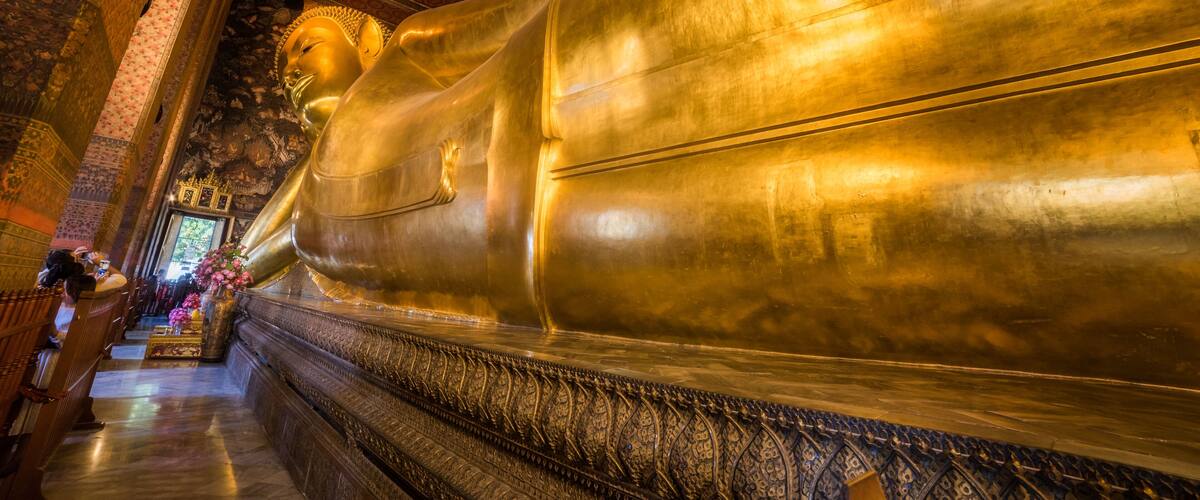 A large golden Buddha statue in a temple with intricate carvings and a patterned ceiling.