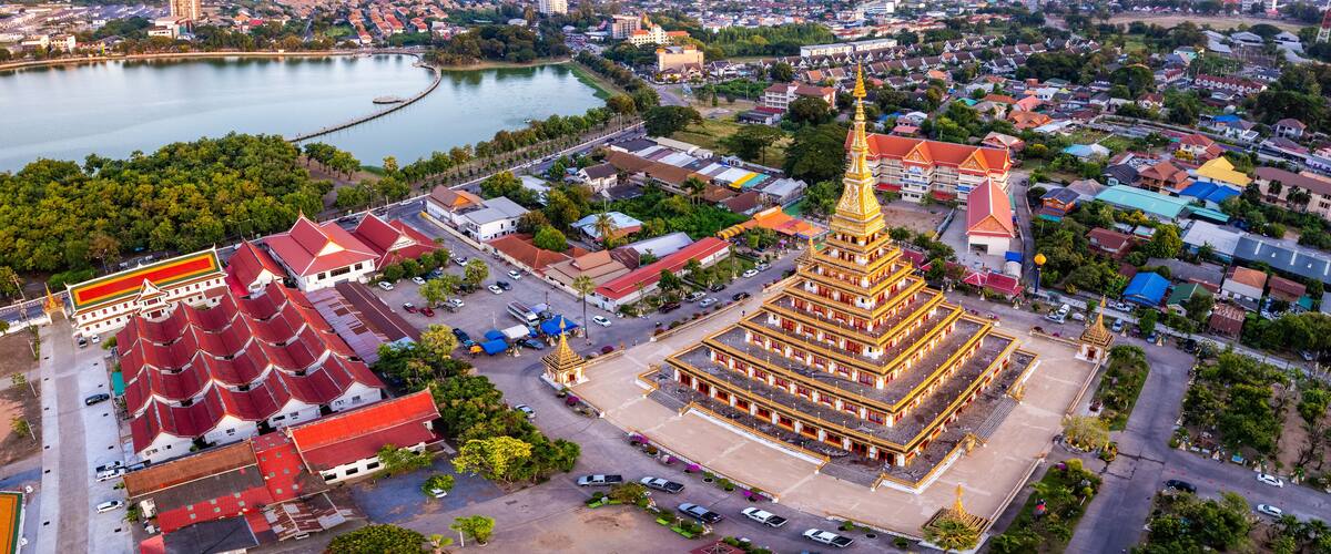 An aerial view of a city with a prominent golden pagoda, a large temple with red roofs, and a calm lake.