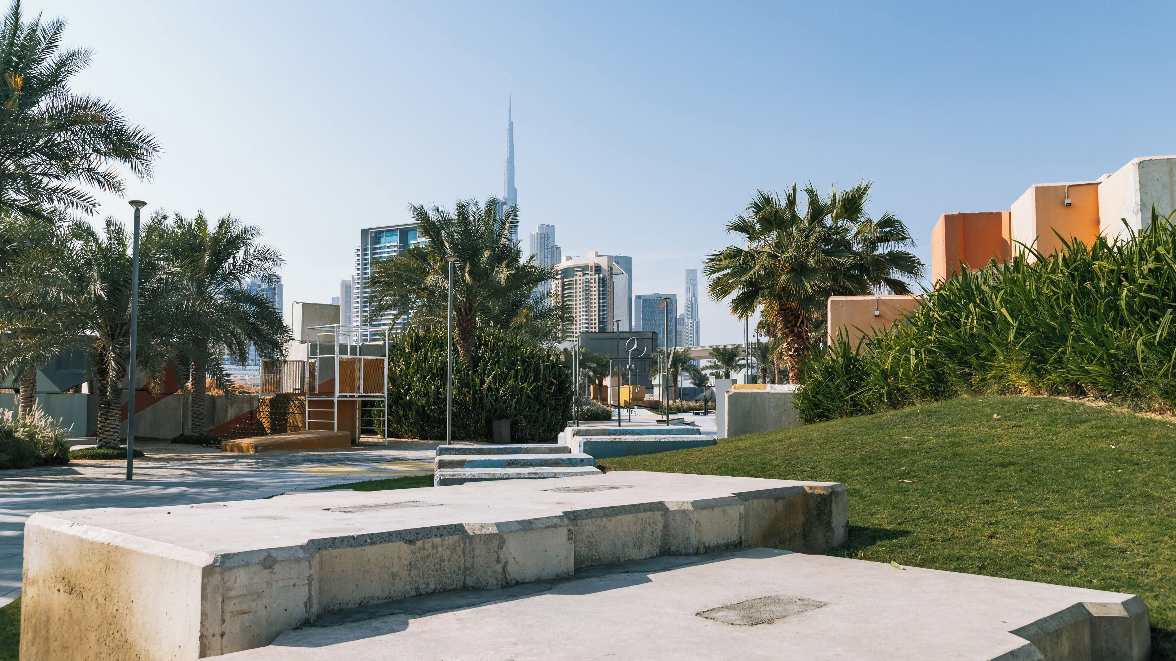 A cityscape with modern buildings, palm trees, and a concrete plaza.