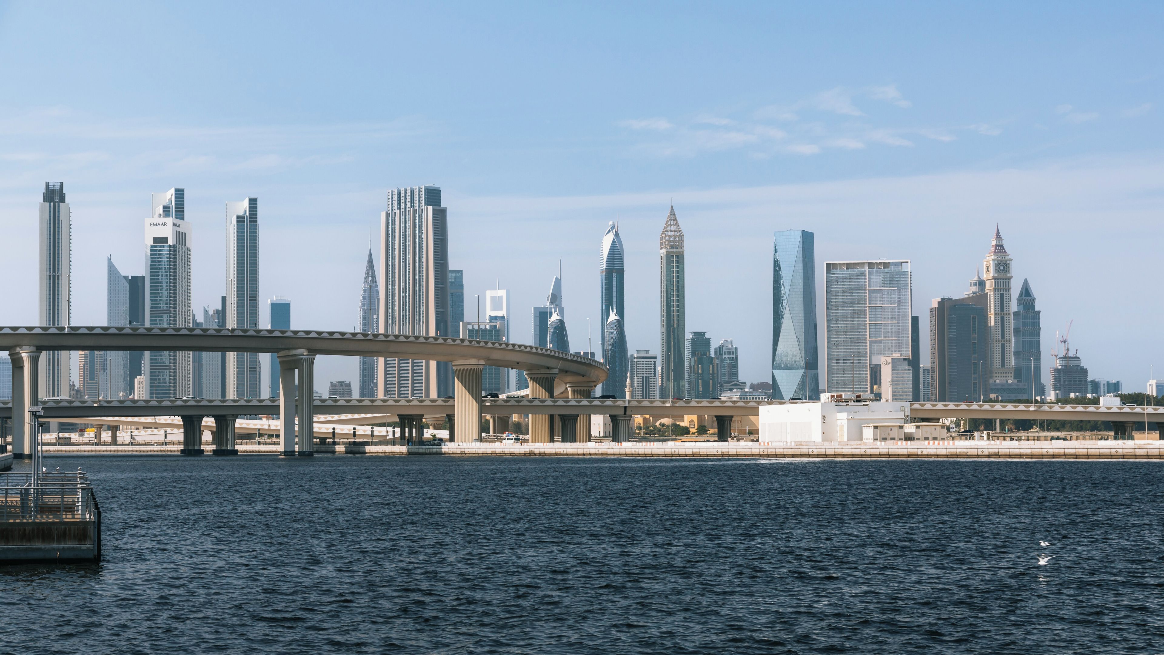 A city skyline with modern skyscrapers, a bridge over water, and a clear sky.