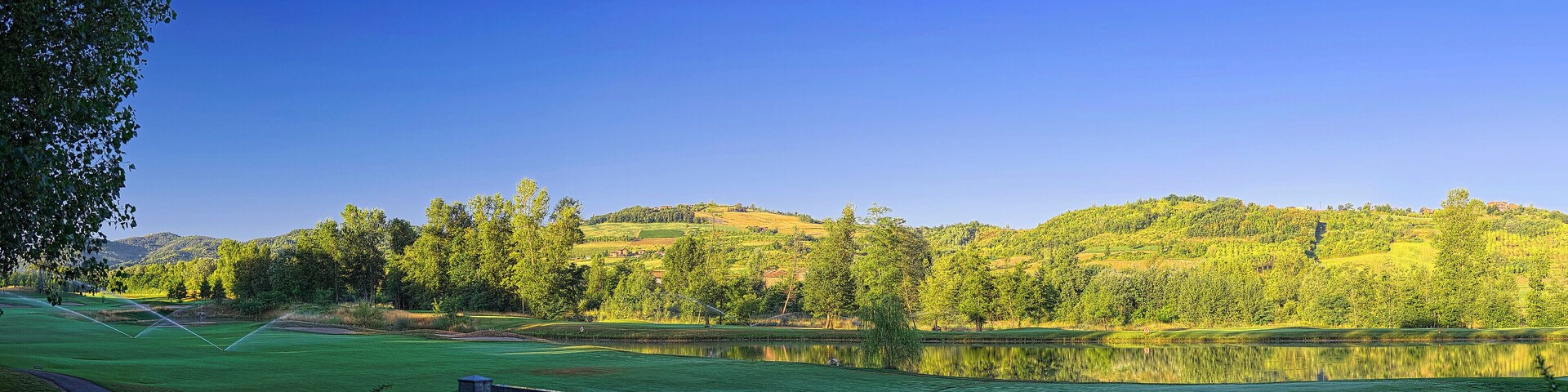 Un campo de golf con un lago, rodeado de árboles y colinas.