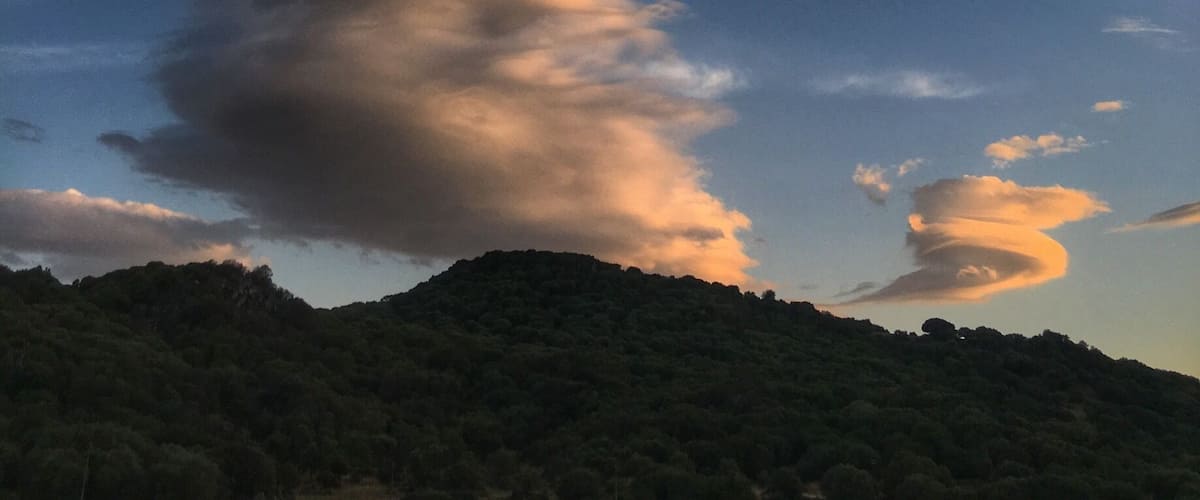 A mountain with a cloud formation against a blue sky.