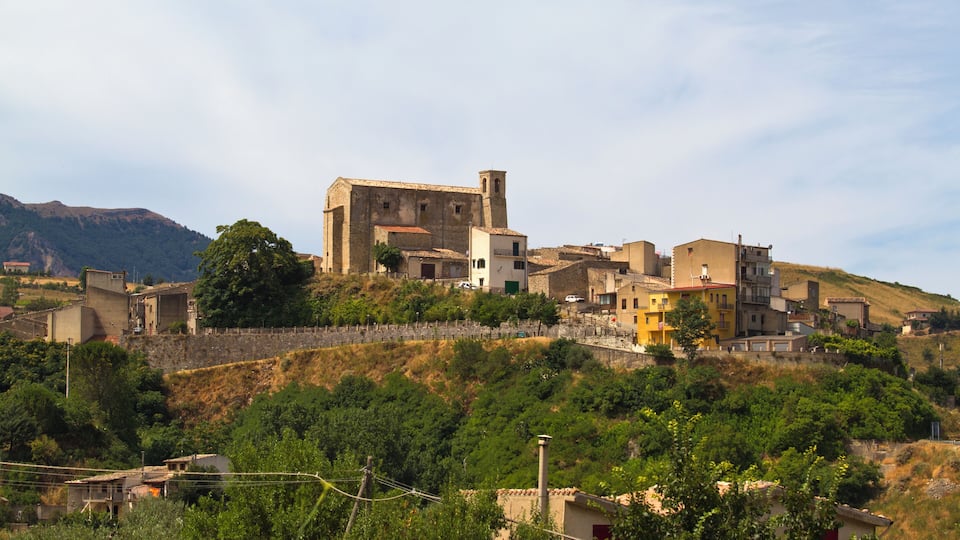 A historic town with a prominent church and tower, surrounded by lush greenery and hills.