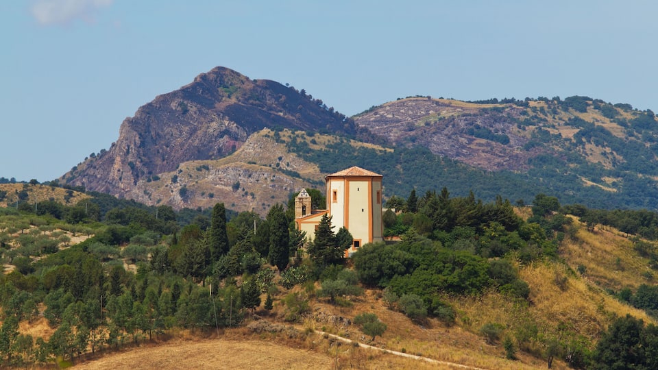 A church with a bell tower surrounded by trees and hills.