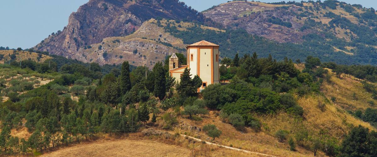 A church with a bell tower surrounded by trees and hills.