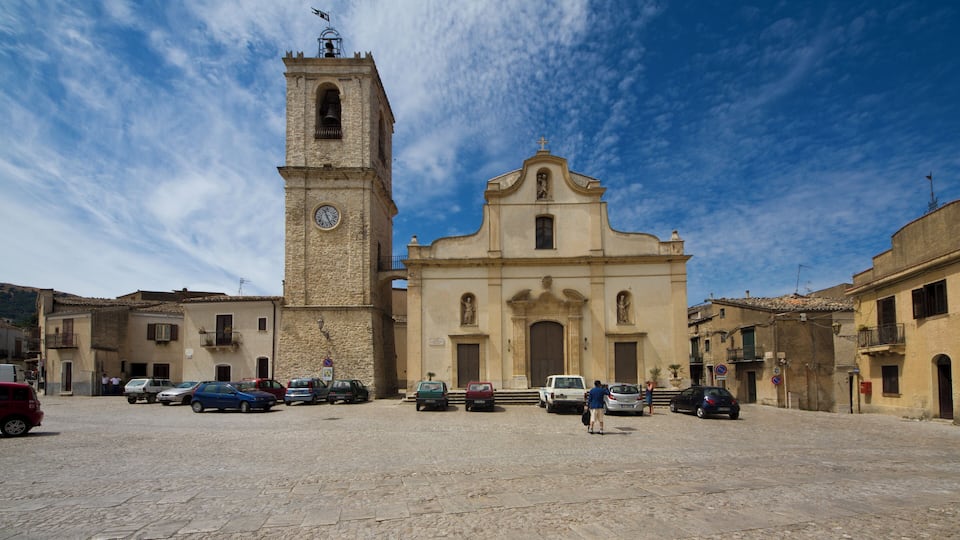 A historic church with a bell tower and a clock, surrounded by cobblestone streets and parked cars.