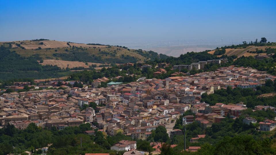 A densely packed town with red-roofed buildings nestled in a green valley.