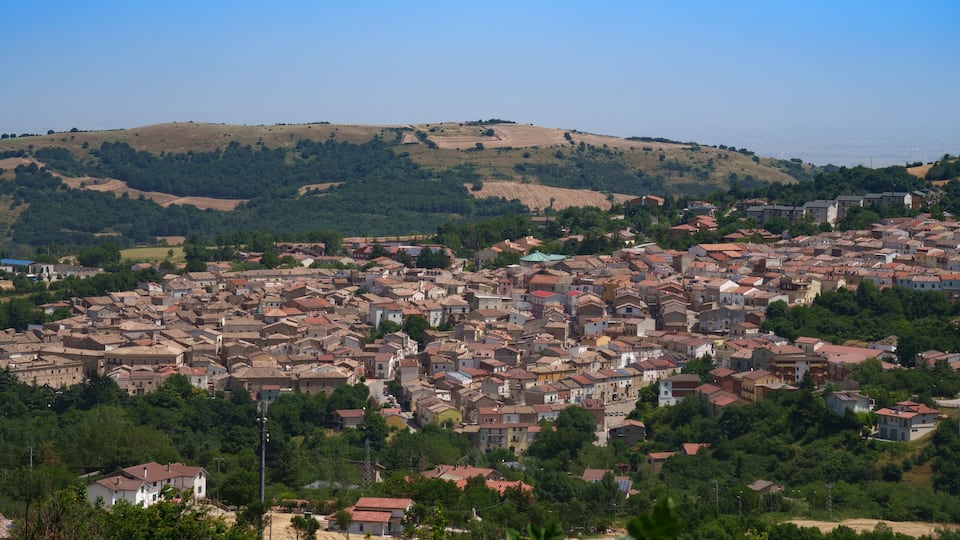 A town with densely packed buildings, surrounded by green hills and trees.