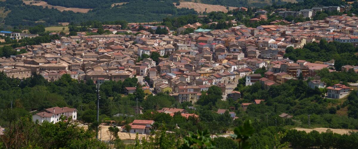 A town with densely packed buildings, surrounded by green hills and trees.