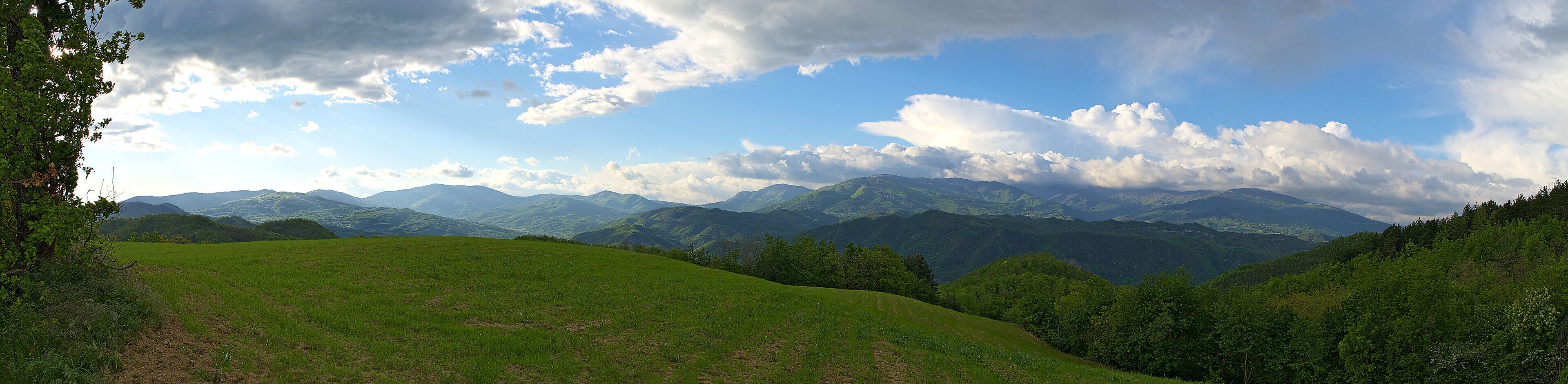 A mountainous landscape with rolling hills, dense forests, and a partly cloudy sky.