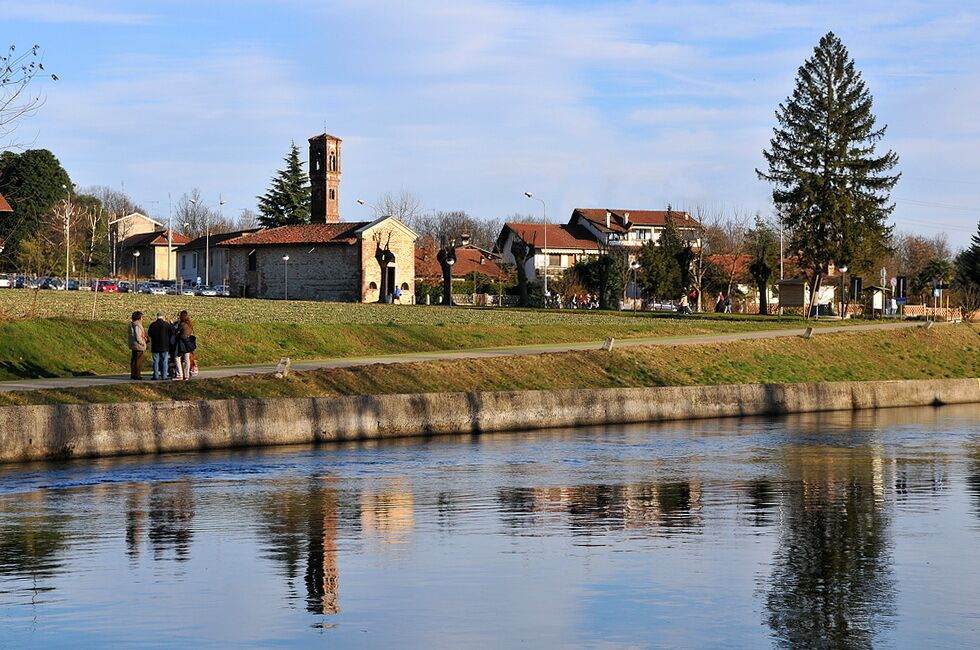 A riverside view with a stone bridge, a church with a bell tower, and residential buildings.