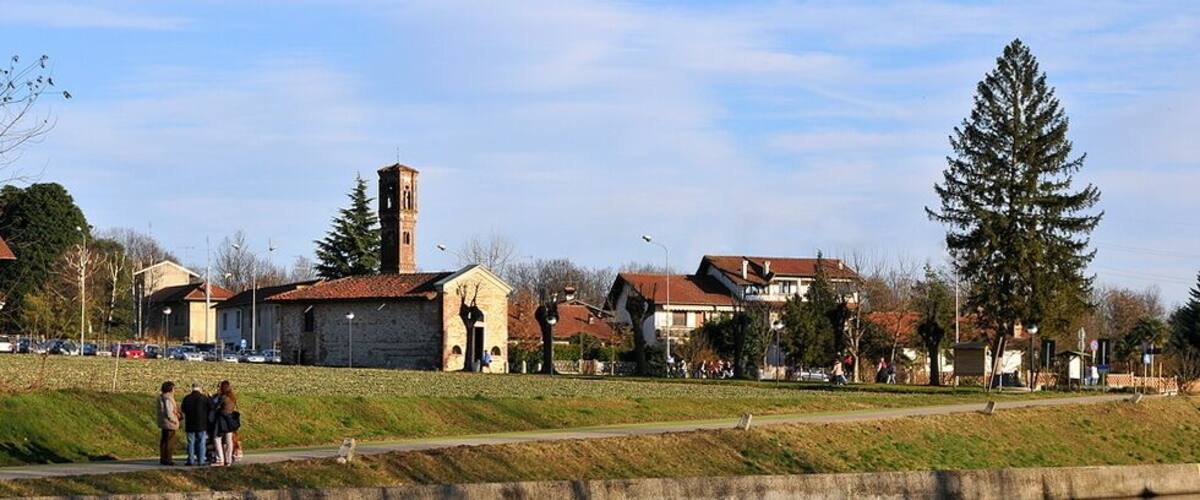 A riverside view with a stone bridge, a church with a bell tower, and residential buildings.
