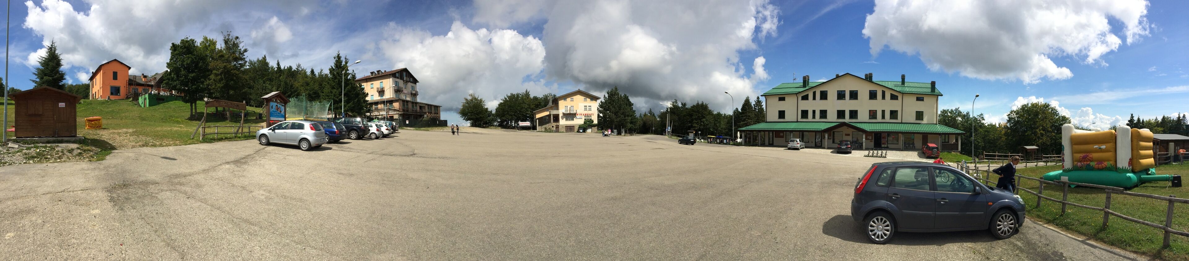 A parking lot with several cars, a small wooden structure, and buildings with green roofs.