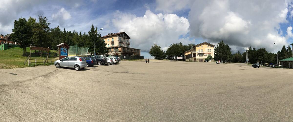A parking lot with several cars, a small wooden structure, and buildings with green roofs.