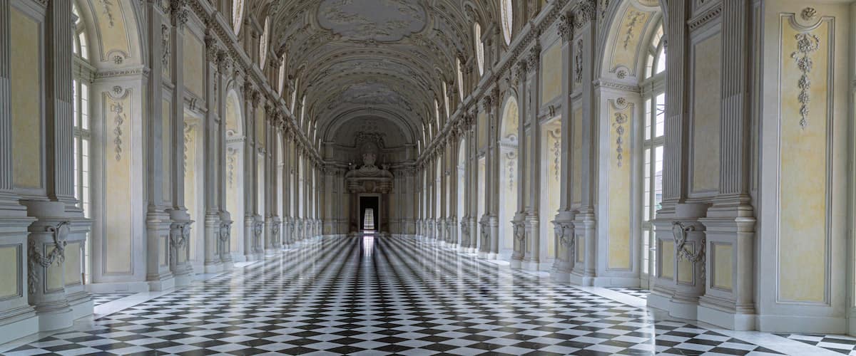 Un maestoso ingresso con pavimento a scacchi, colonne decorate e un soffitto alto con decorazioni elaborate.