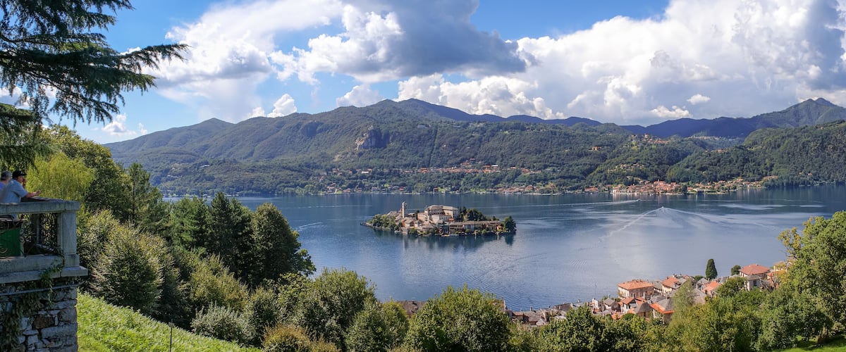 A lake surrounded by mountains, a small island with buildings, and a town in the foreground.