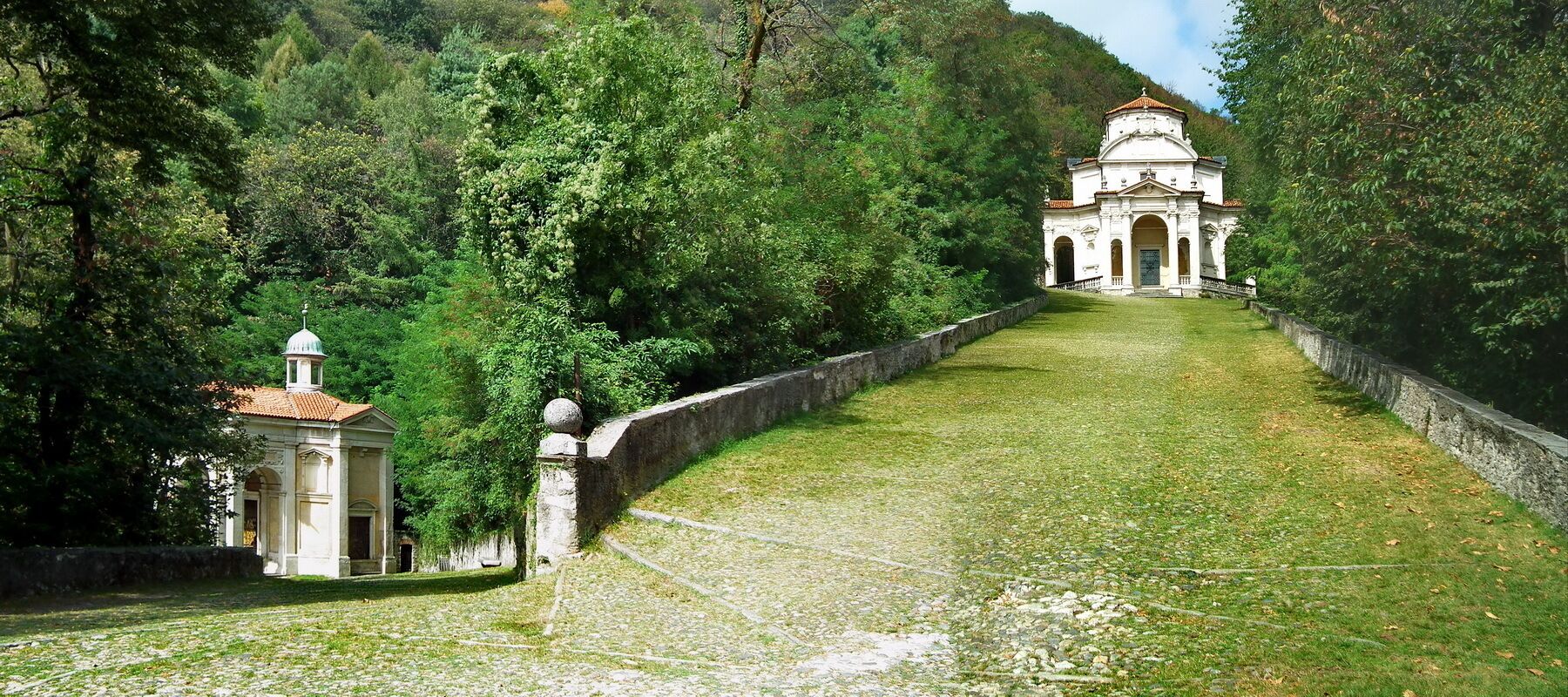 A pathway leading to a white church with a dome, surrounded by lush greenery and trees.
