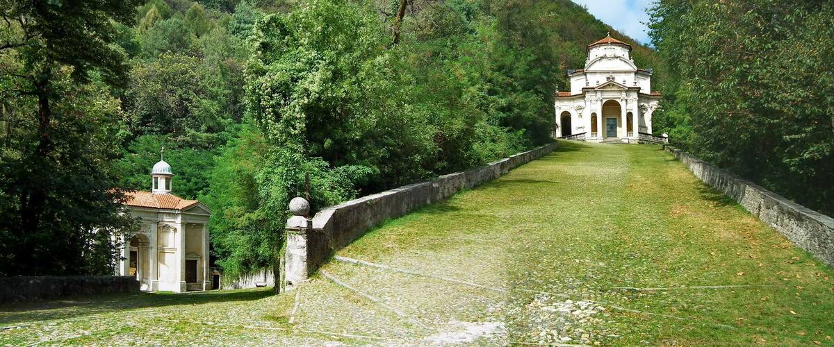 A pathway leading to a white church with a dome, surrounded by lush greenery and trees.