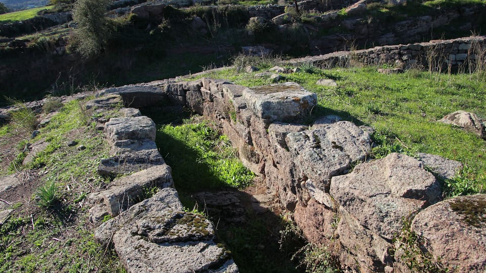 Ancient stone ruins with a narrow passageway surrounded by grassy terrain and scattered rocks.