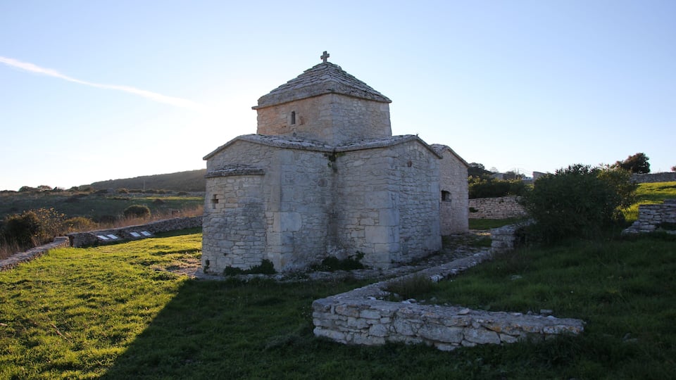 An old stone church with a small bell tower surrounded by grassy fields and stone walls.