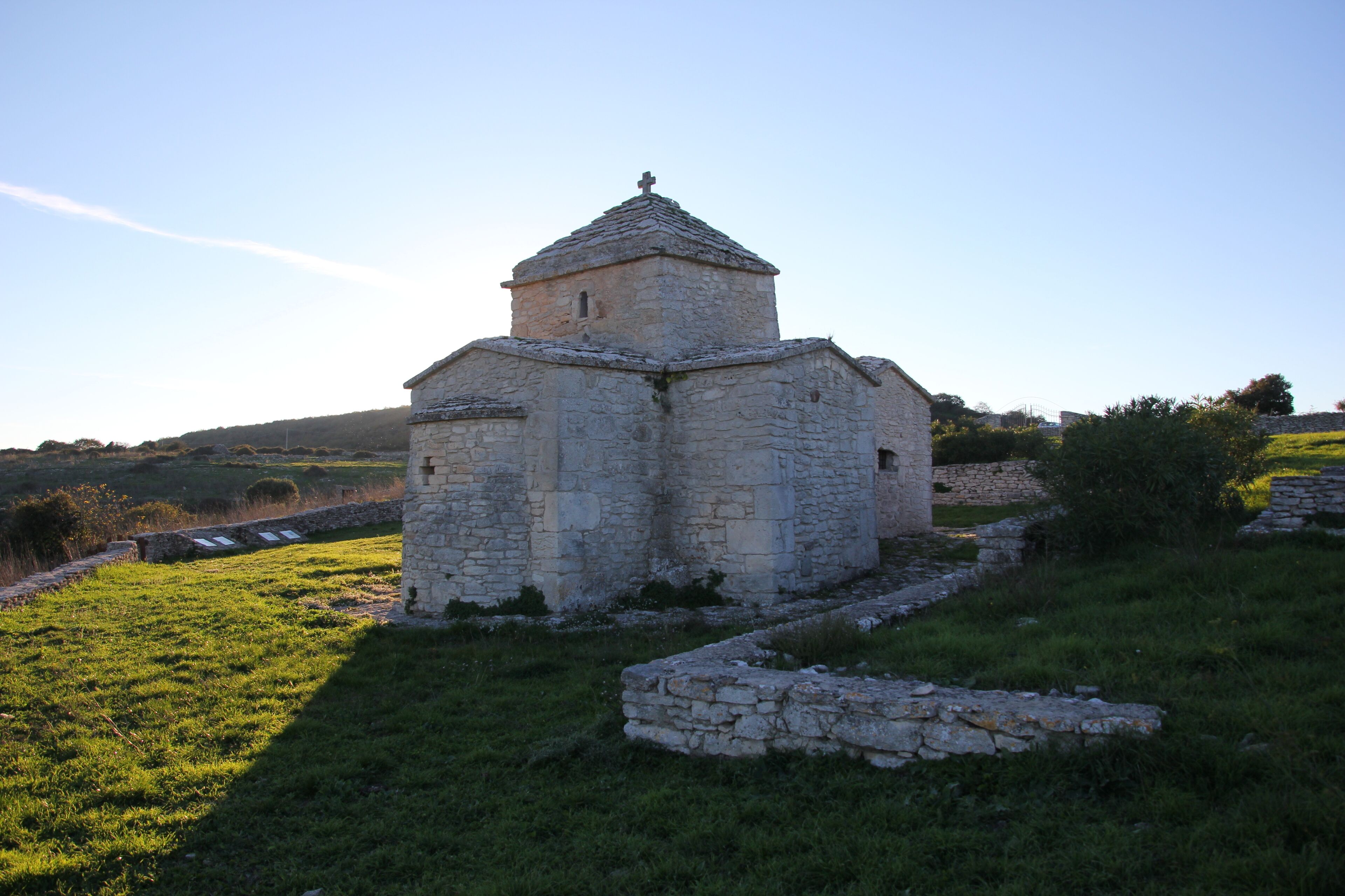 An old stone church with a small bell tower surrounded by grassy fields and stone walls.