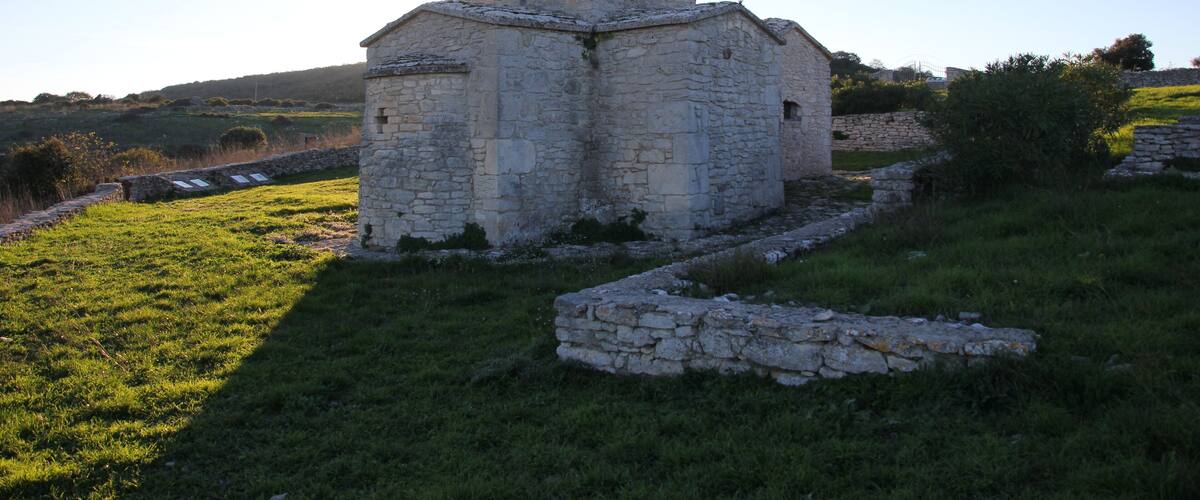 An old stone church with a small bell tower surrounded by grassy fields and stone walls.