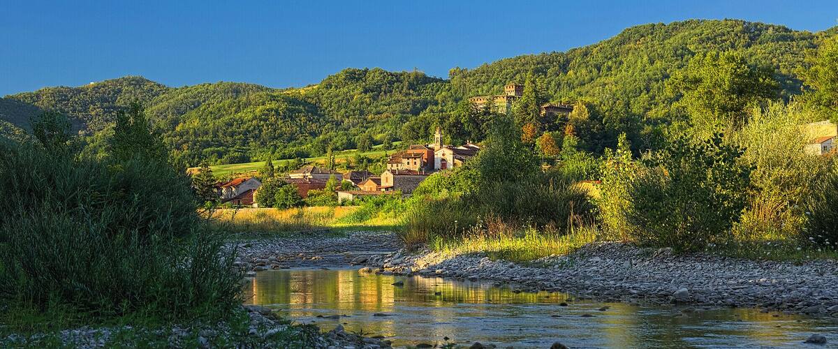 A river with a rocky bed, surrounded by lush greenery and a village with traditional buildings on a hillside.