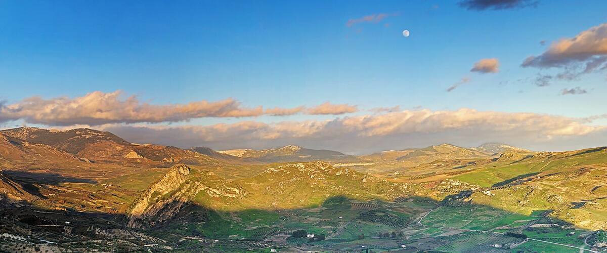 A mountainous landscape with a valley, a small settlement, and a visible moon.