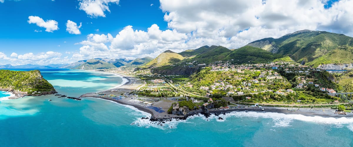 A coastal town with a beach, mountains, and clear blue waters.