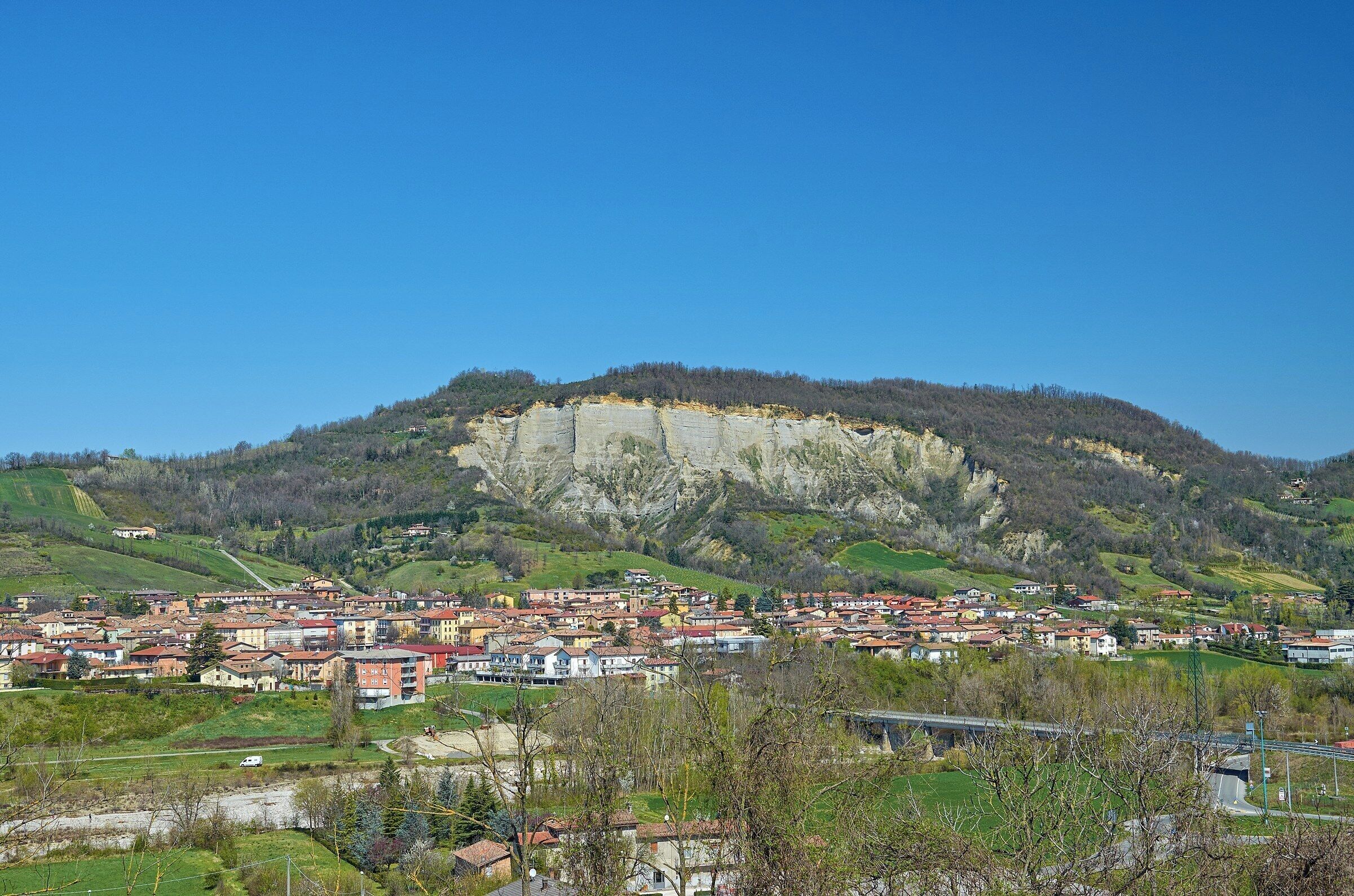 A town nestled at the base of a large cliff, with a clear blue sky above.