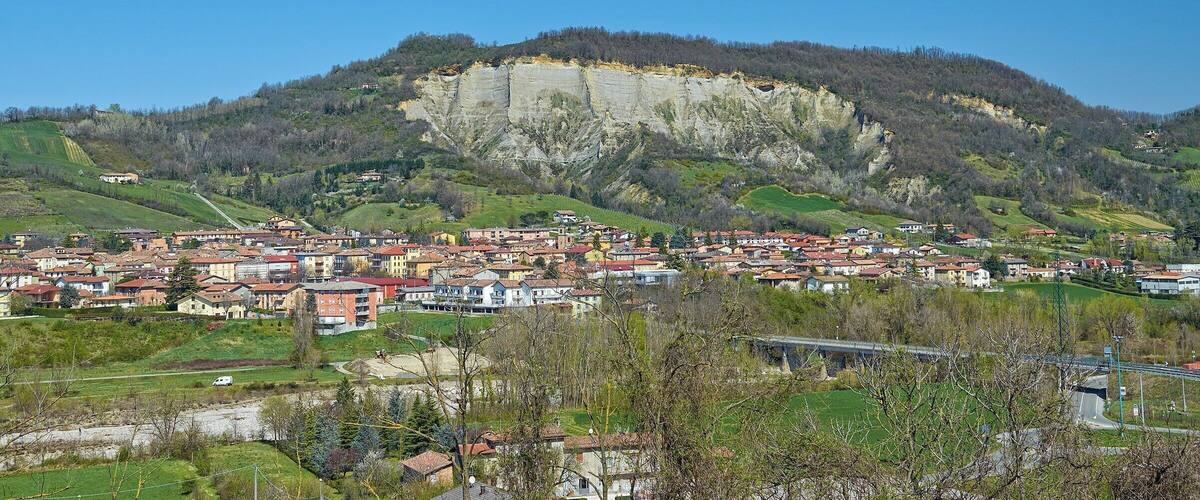 A town nestled at the base of a large cliff, with a clear blue sky above.