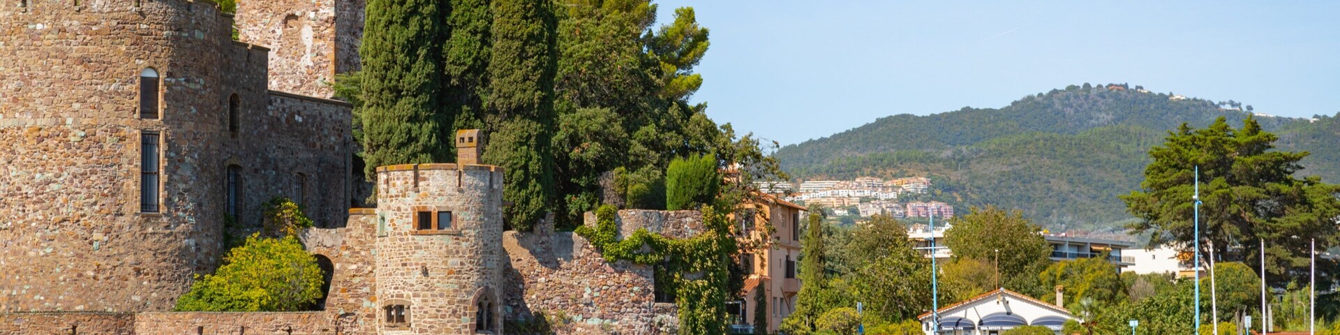 A historic stone castle with towers, a beach, and a hillside town in the background.