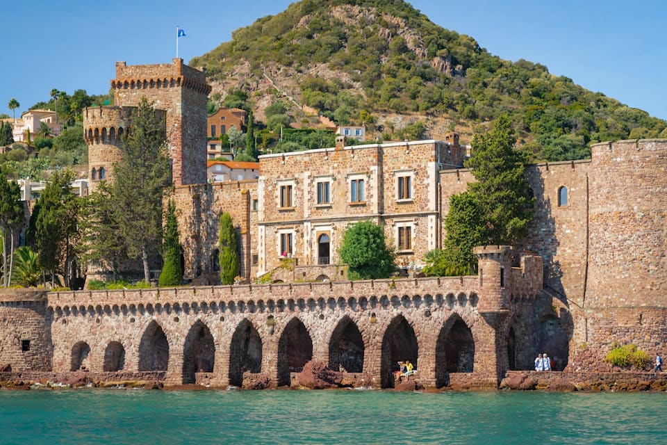 A historic stone fortress with a tower, arched walkways, and a hillside backdrop.
