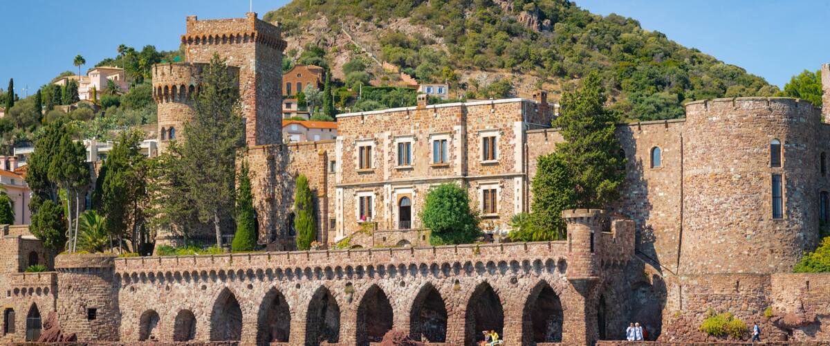 A historic stone fortress with a tower, arched walkways, and a hillside backdrop.