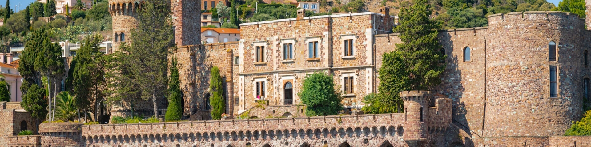 A historic stone fortress with a tower, arched walkways, and a hillside backdrop.