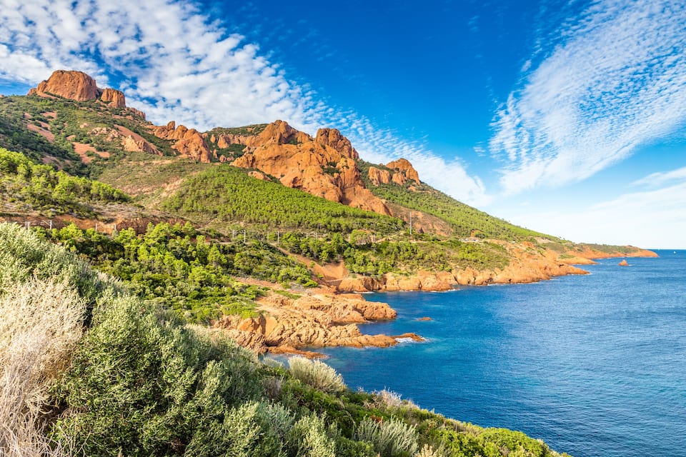 A coastal landscape with rocky cliffs, green vegetation, and a clear blue sea.