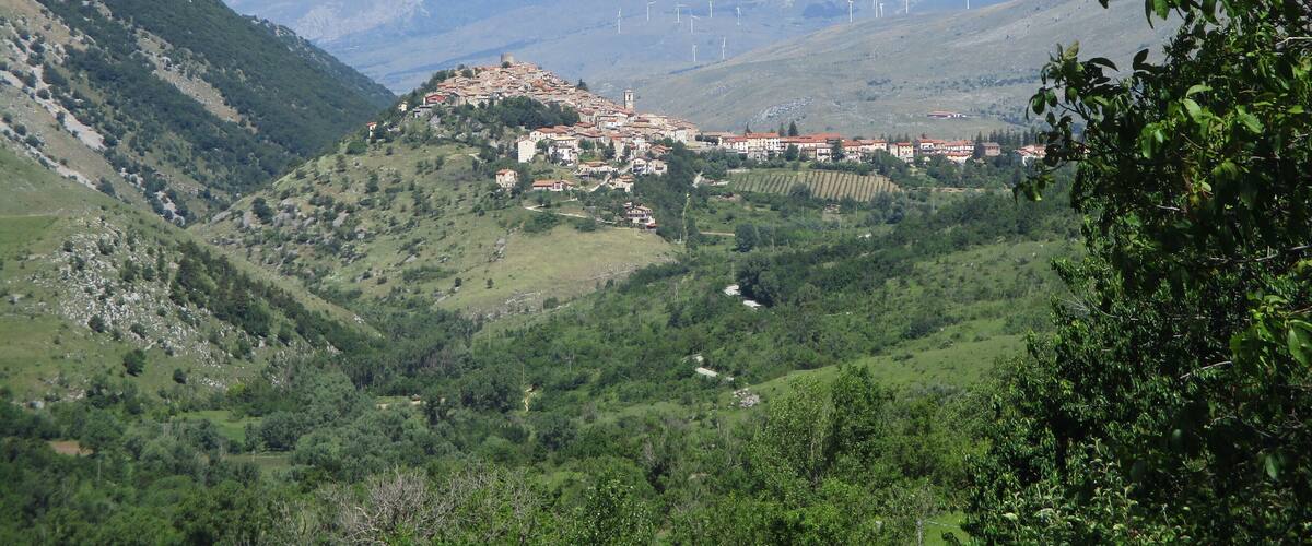 A mountainous landscape with a village, green valleys, and wind turbines in the distance.