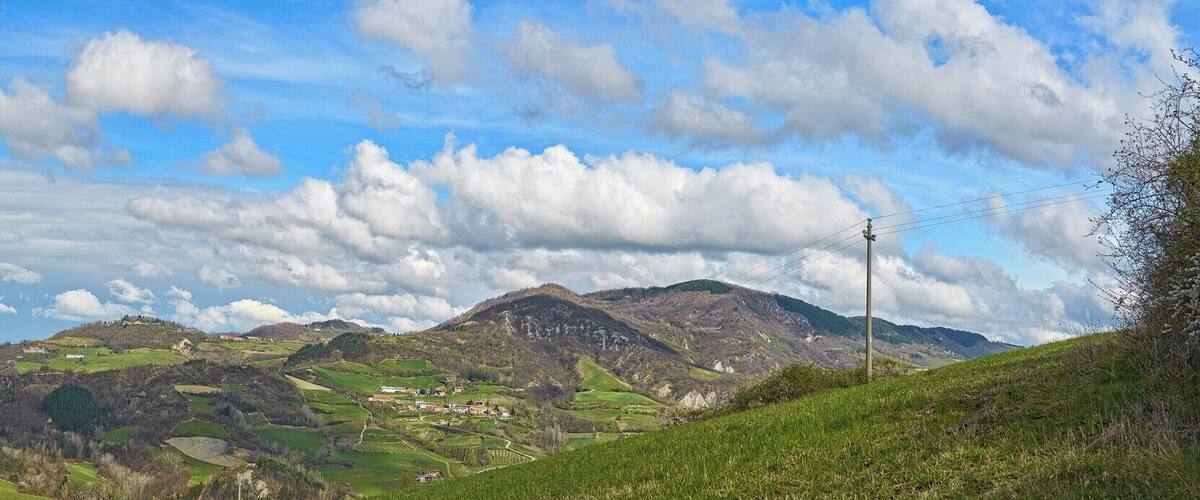 A mountainous landscape with rolling hills, scattered houses, and a clear blue sky with clouds.