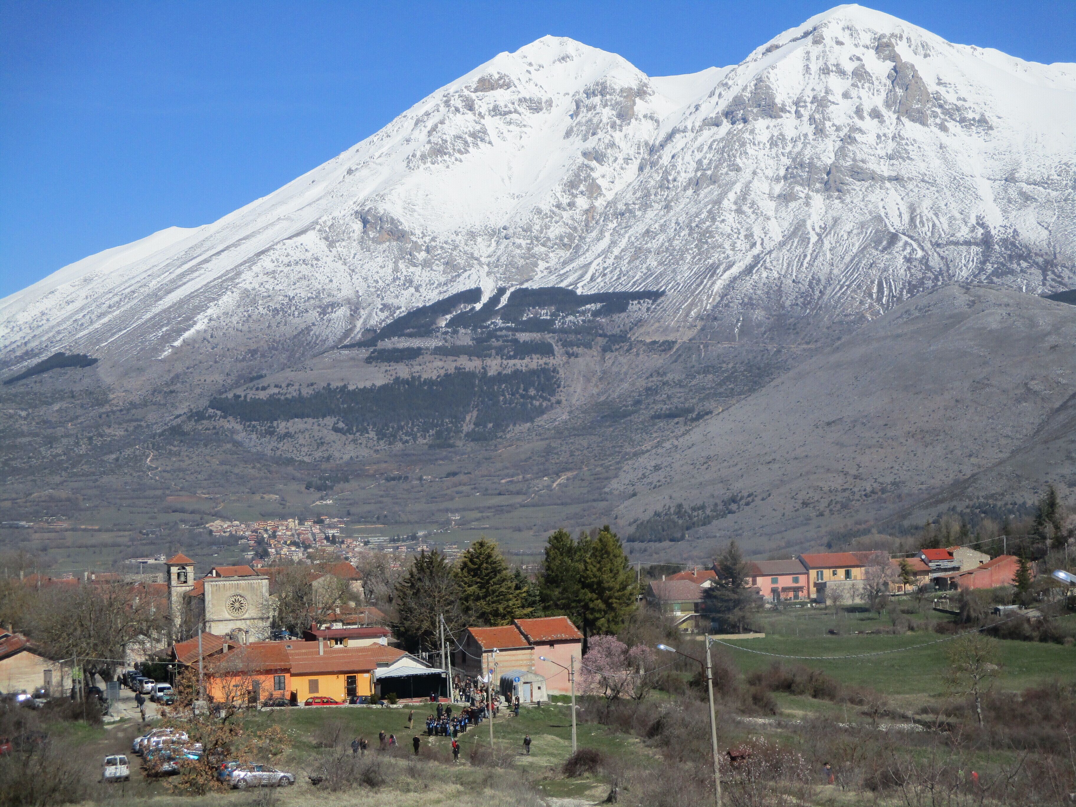 A snow-covered mountain, a town with buildings, and a clear blue sky.