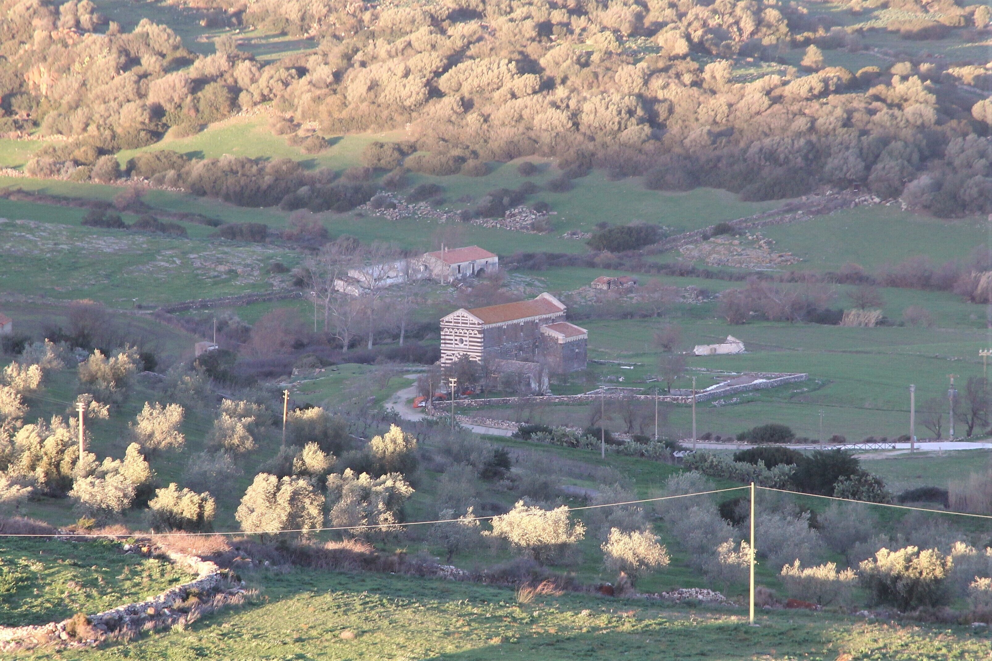 A rural landscape with a large stone building surrounded by fields and trees.