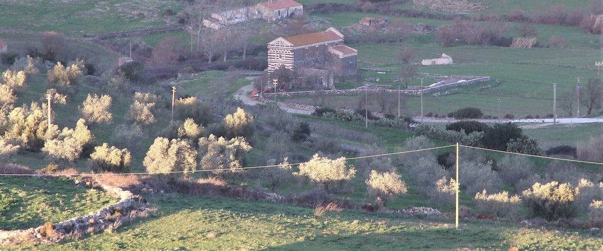 A rural landscape with a large stone building surrounded by fields and trees.