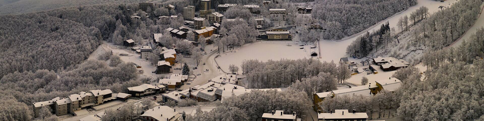 A snow-covered village nestled in a mountainous area with a mix of residential buildings and a large central structure.