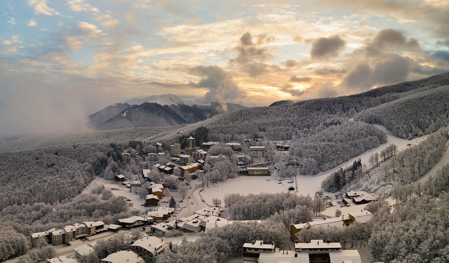 A snow-covered village nestled in a mountainous area with a mix of residential buildings and a large central structure.