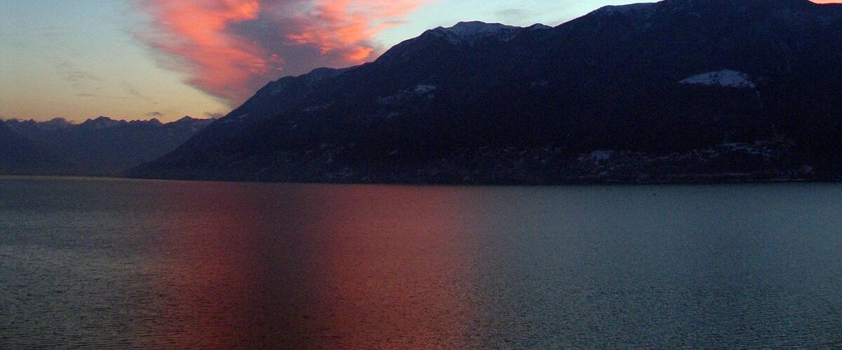 A mountain range with a lake in the foreground and a sunset sky.