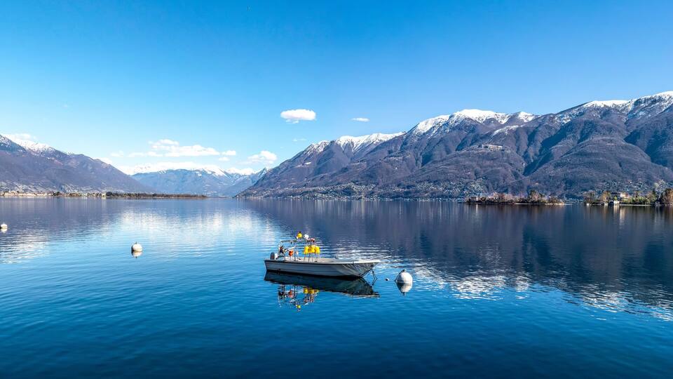 A calm lake with a boat, snow-capped mountains, and a small town on the shore.