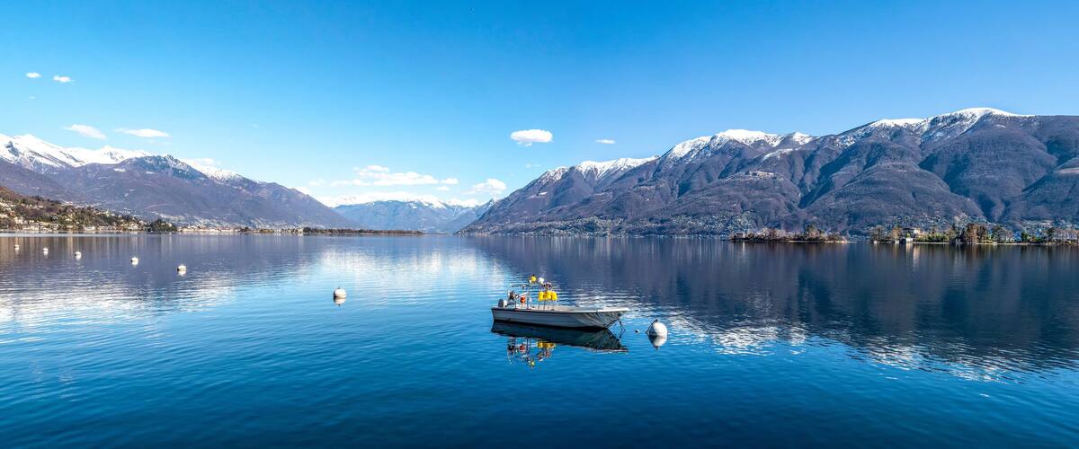 A calm lake with a boat, snow-capped mountains, and a small town on the shore.