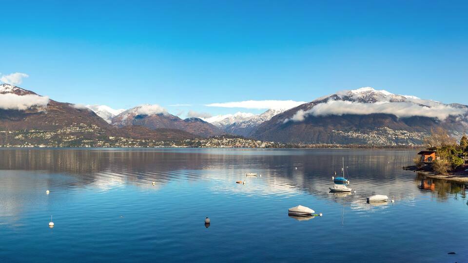 A calm lake with boats, snow-capped mountains, and a town in the background.