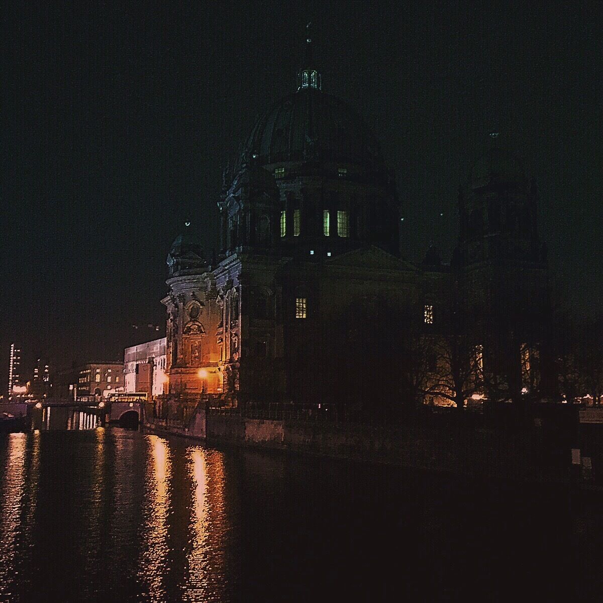 A nighttime view of a historic building with a dome and illuminated windows, reflecting on a body of water.
