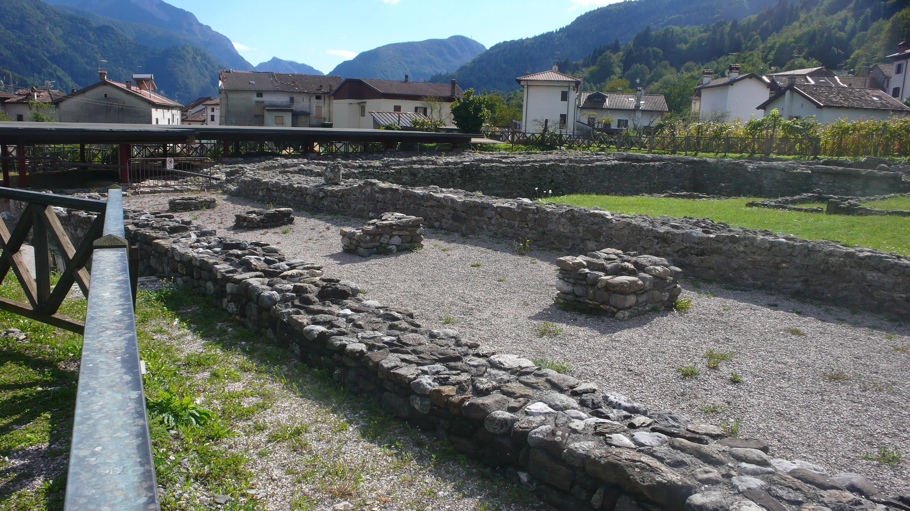 Ancient stone ruins with a wooden fence and houses in the background.